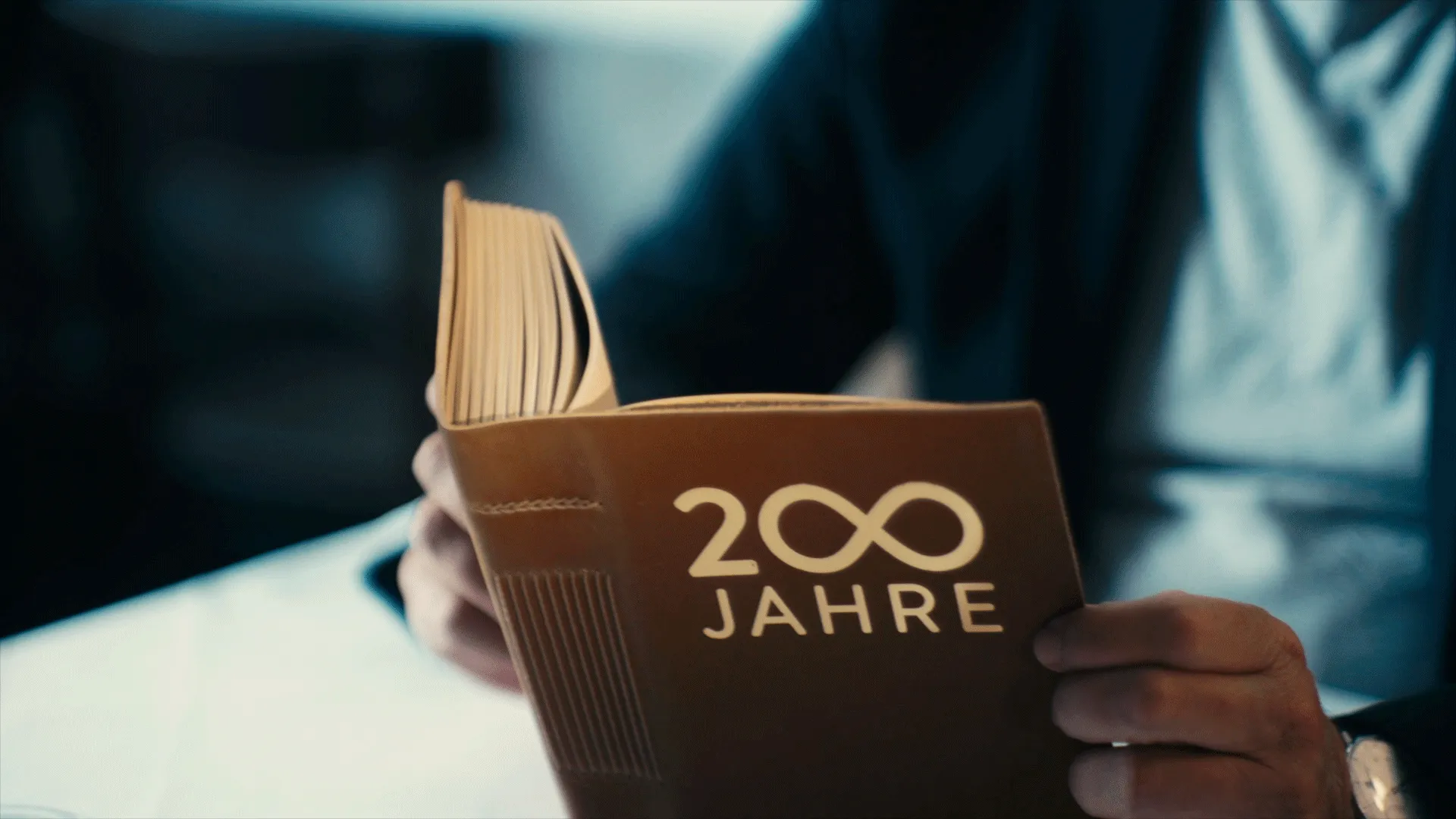 Eine Person hält ein aufgeschlagenes Buch mit dem Schriftzug '200 Jahre' auf dem Einband.