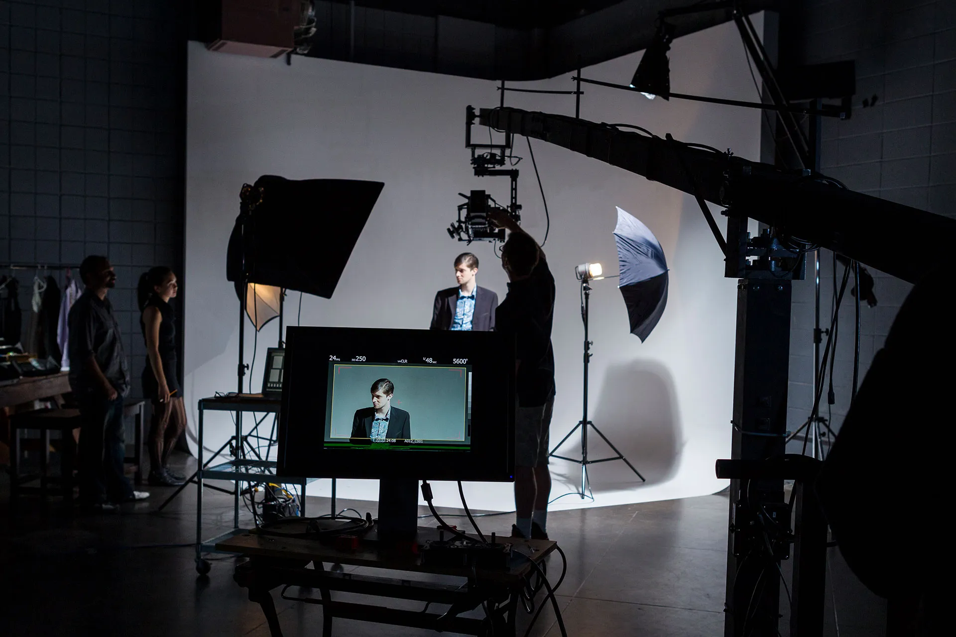 Fotoshooting im Studio mit männlichem Model vor weißem Hintergrund und Kameramann, der Kameraeinstellungen anpasst.