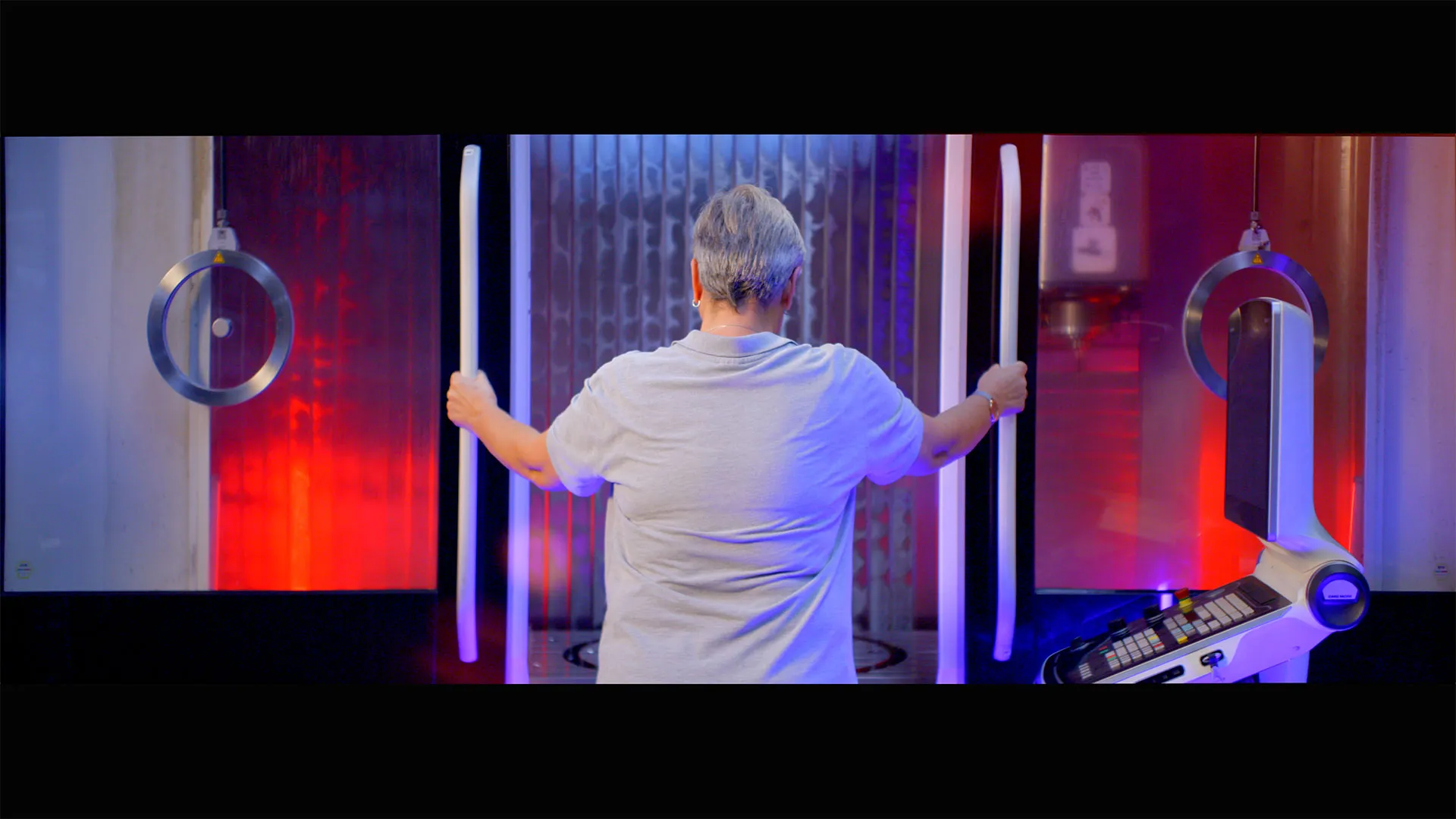 Person von hinten hält zwei lange, leuchtende Stäbe vor einem futuristisch aussehenden Gerät mit roten und blauen Lichtern.