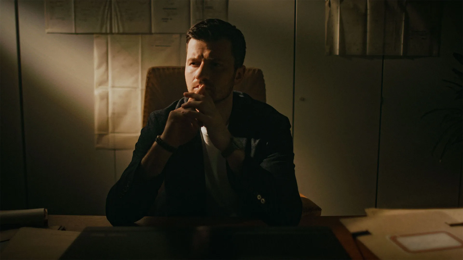 Mann sitzt nachdenklich an einem Schreibtisch in einem dunklen Raum mit schwachem Licht.