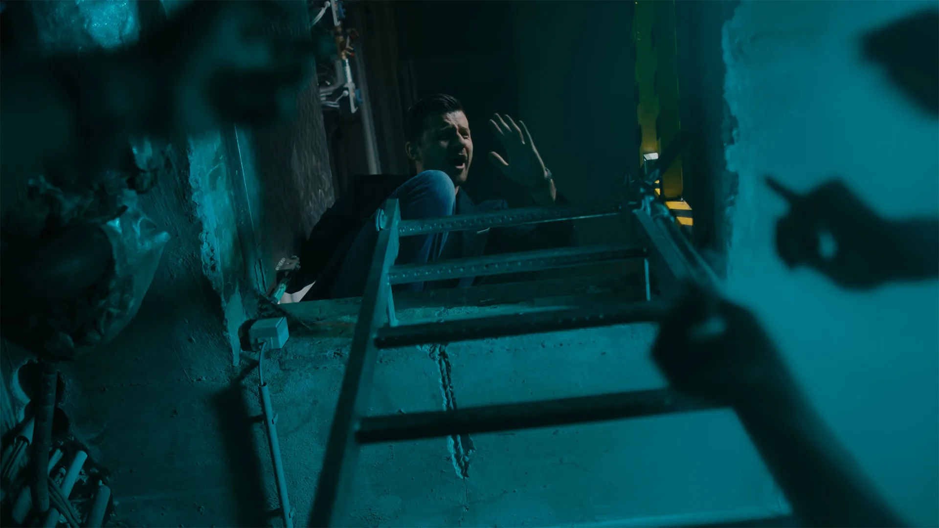 Mann klettert eine Metallleiter hinauf und hebt die Hand, während eine weitere Hand von unten auf ihn zeigt.