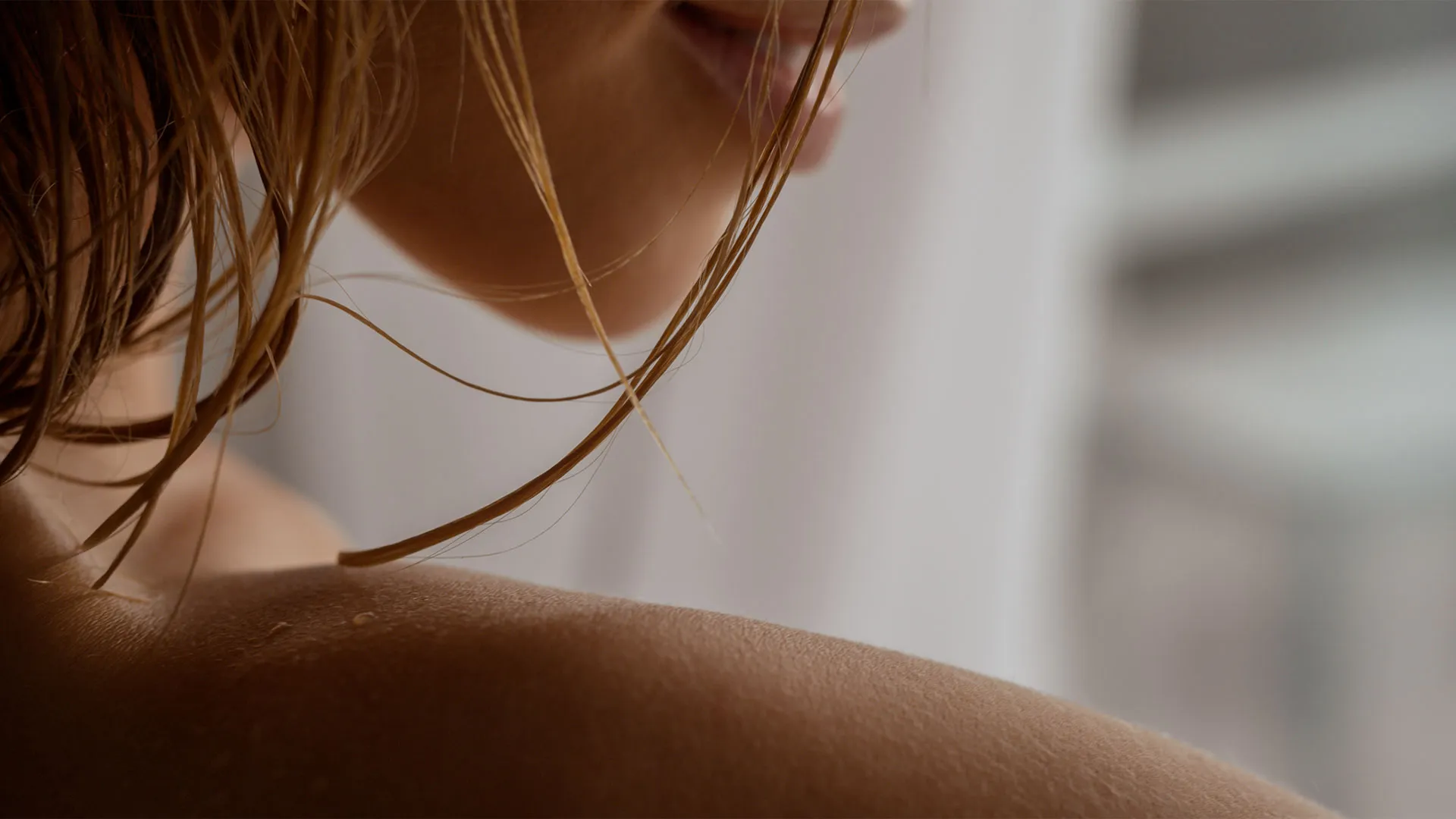 Nahaufnahme einer lächelnden Frauenkehle mit feuchten, herabfallenden Haarsträhnen über der Schulter.