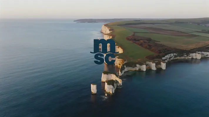 Luftaufnahme der weißen Kreidefelsen entlang der Küste mit grünem Ackerland im Hintergrund.