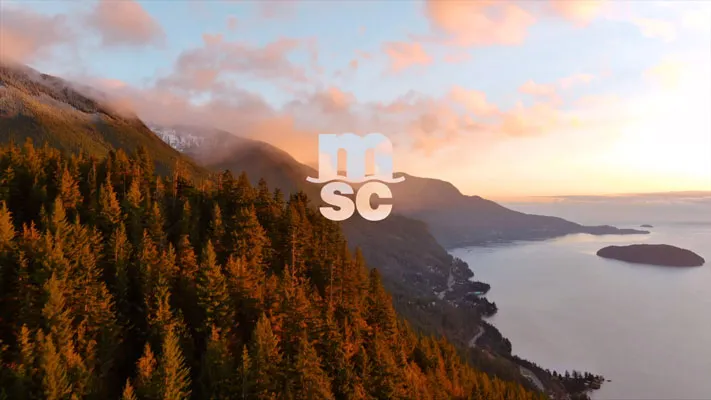 Sonnenuntergang über bewaldeten Bergen mit Blick auf einen ruhigen See und eine kleine Insel.