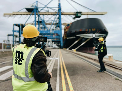 Videoproduktion am Hafen: Filmcrew mit Warnwesten dreht Szenen vor einem großen Containerschiff.