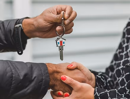 Two people shaking hands while one person passes the other house keys