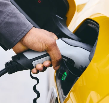 Man charging a yellow electric vehicle purchased with a Tandem motor finance loan.