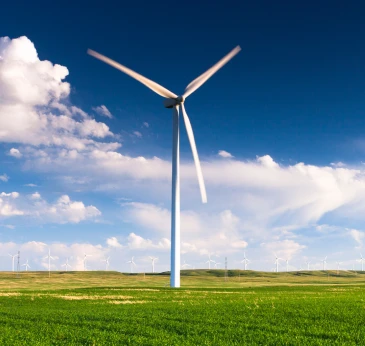 Windmill turbine in the middle of a green field, creating renewable enery for greener homes.