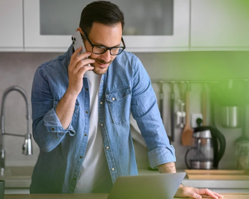 A man standing in his kitchen, on the phone, calling the Tandem Customer Support about his account.