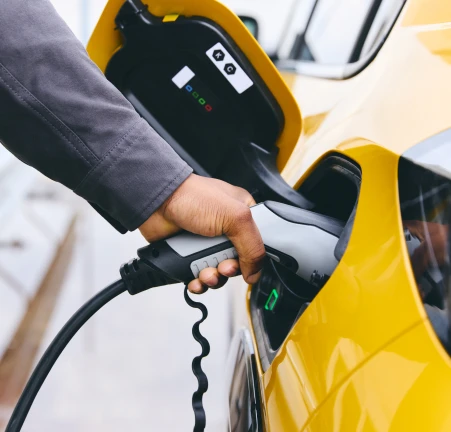 Man charging a yellow electric vehicle purchased with a Tandem motor finance loan.