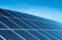 Bright blue solar panels on a red brick UK house roof with a light blue sky in the background.