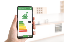 Hand holding a smart phone displaying a home EPC rating of A+ with a blurred kitchen visible in the background.
