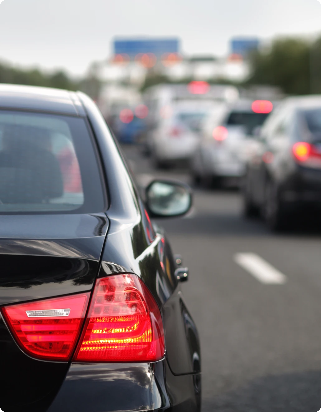 Close-up behind a sleek, low-emission black car, with a blurred background revealing congested traffic on a highway.