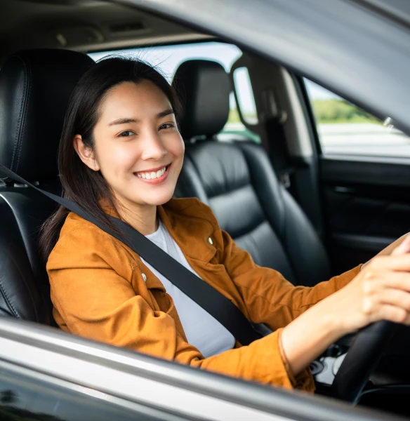 A smiling young lady sitting in the driver's seat of her lower emission vehicle, purchased through Tandem Motor Finance.