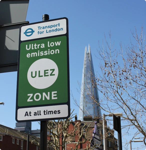 A closeup of a Transport for London ULEZ Zone sign in the heart of London city, with the London Shard visible in the background.