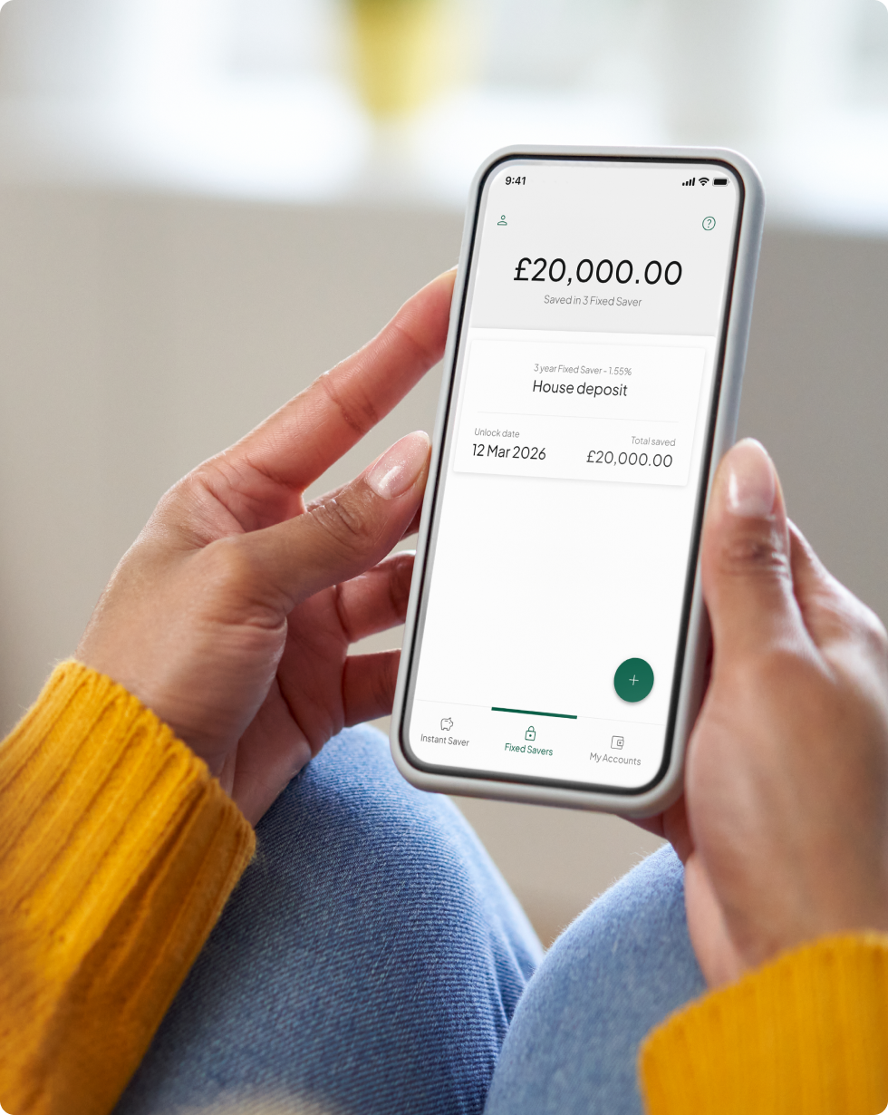 Close-up of a woman's hands holding her smartphone, showcasing the savings securely locked in her Tandem Fixed Saver account displayed on the screen.
