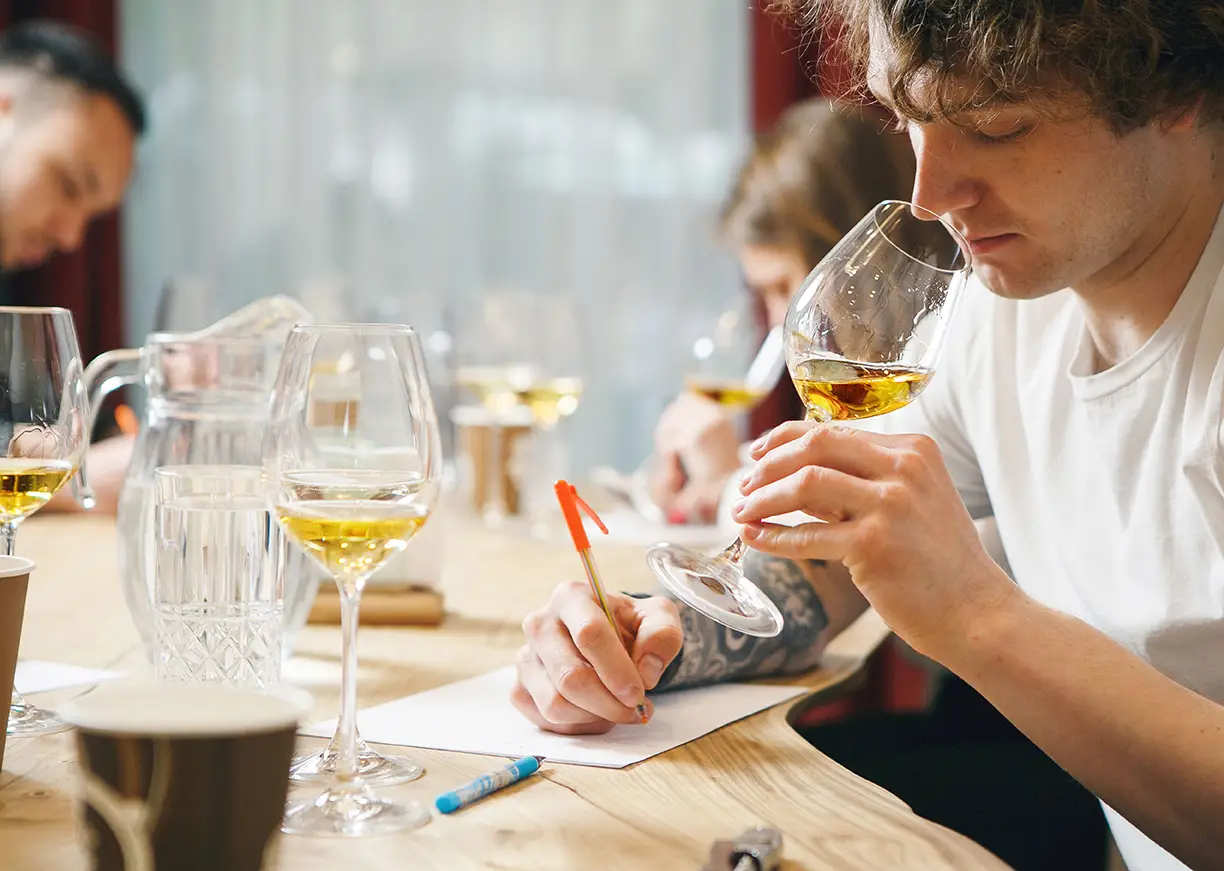 A man writes on paper while sipping a glass of wine