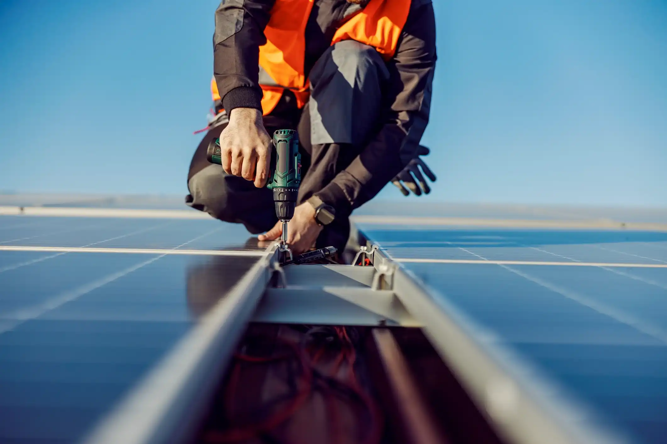 Low-angle view of technician using a drill to install solar panels on a commercial roof