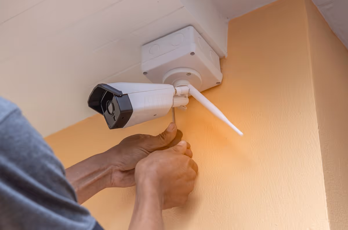 Gros plan d'un technicien fixant une caméra de surveillance sans fil sur un mur.