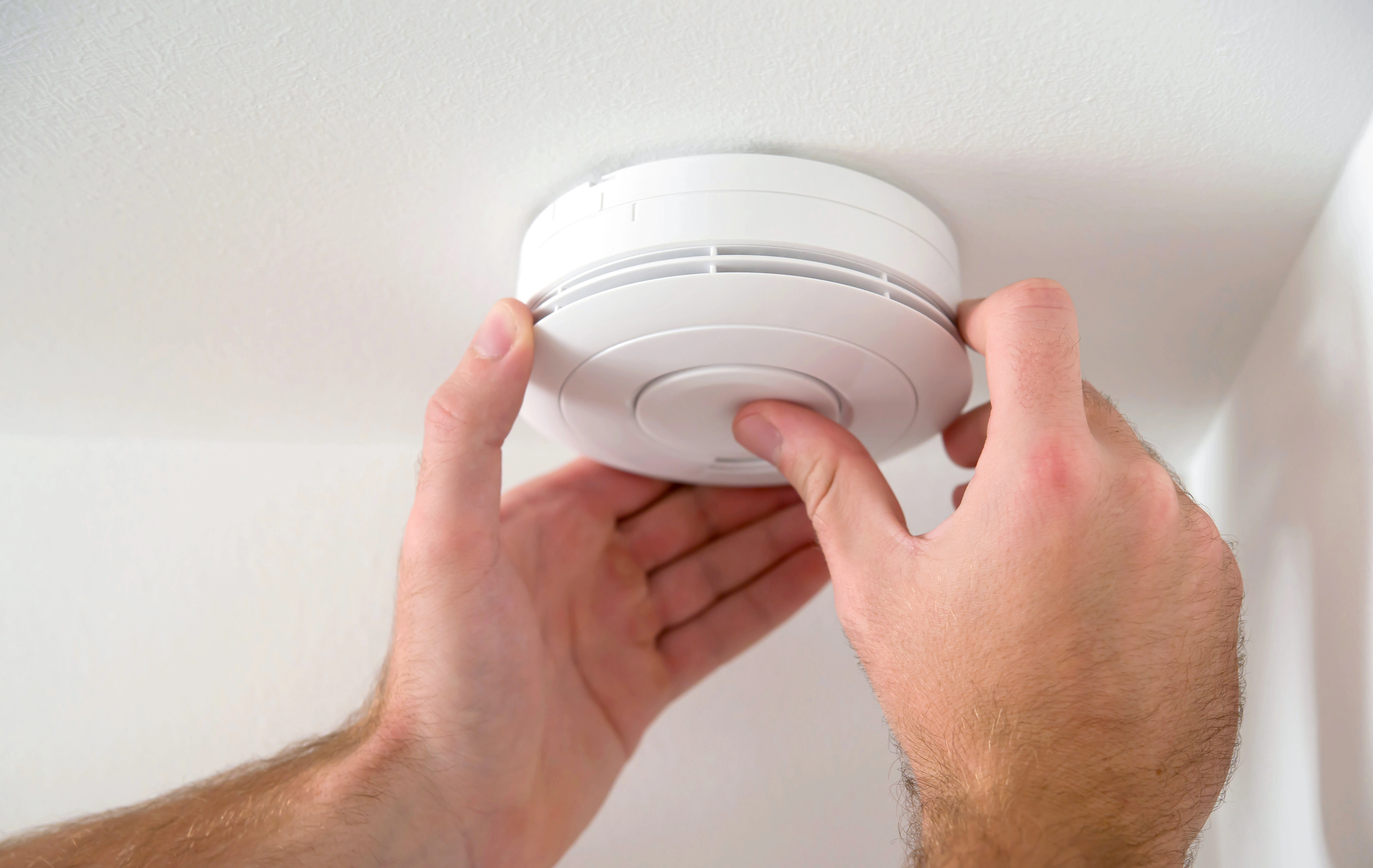 Installateur fixant un détecteur avertisseur au plafond dans le cadre d'une installation d'alarme incendie
