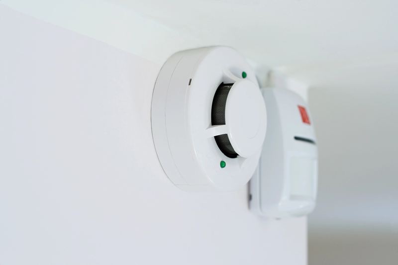 Installateur fixant un détecteur avertisseur au plafond dans le cadre d'une installation d'alarme incendie
