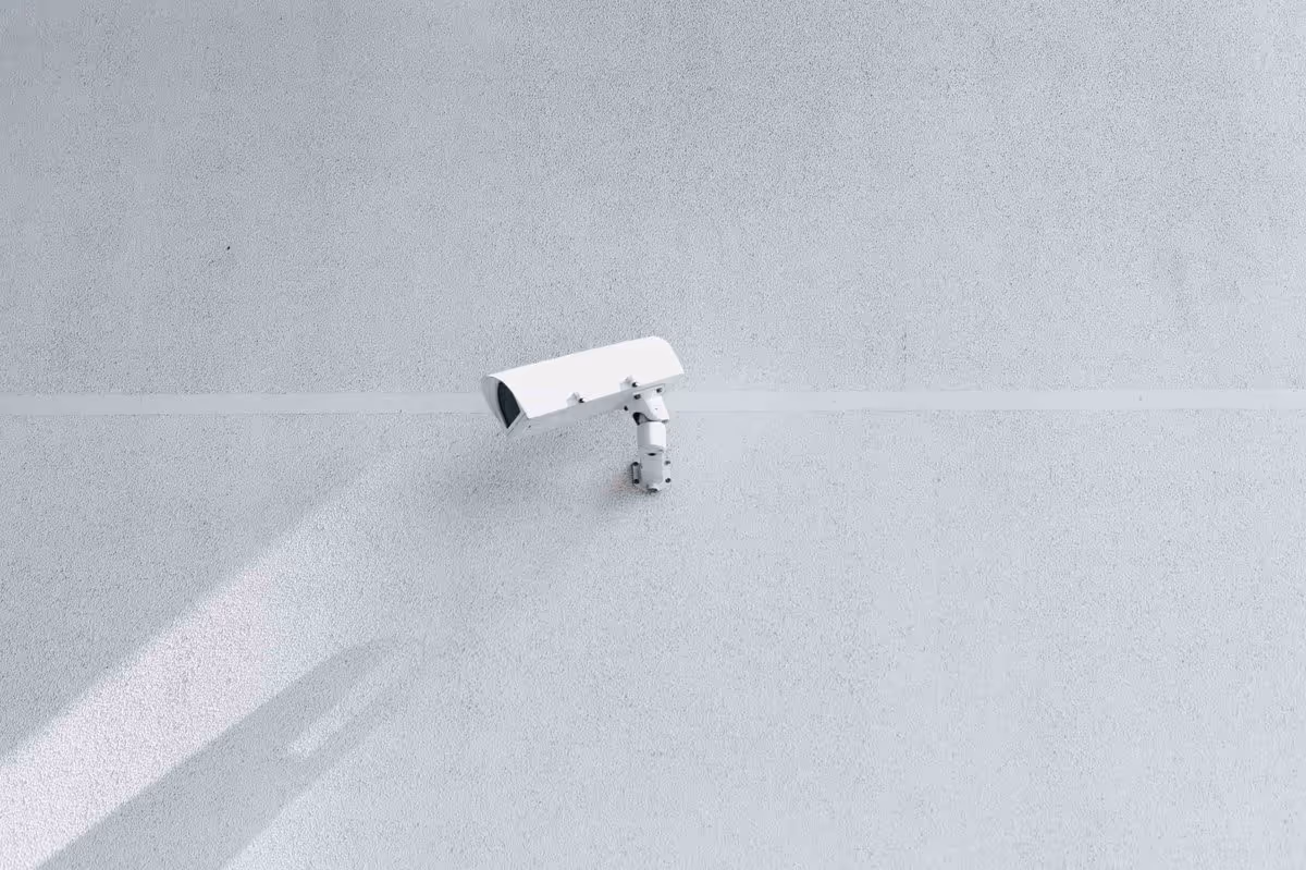 Caméra de vidéosurveillance blanche fixée sur un mur gris minimaliste.