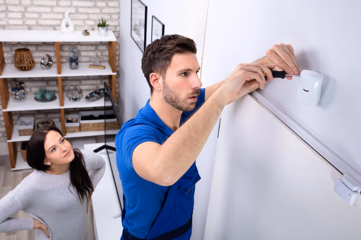 Technicien installant un détecteur de mouvement dans une maison à Colmar pendant qu'une cliente supervise l'installation du système d’alarme.