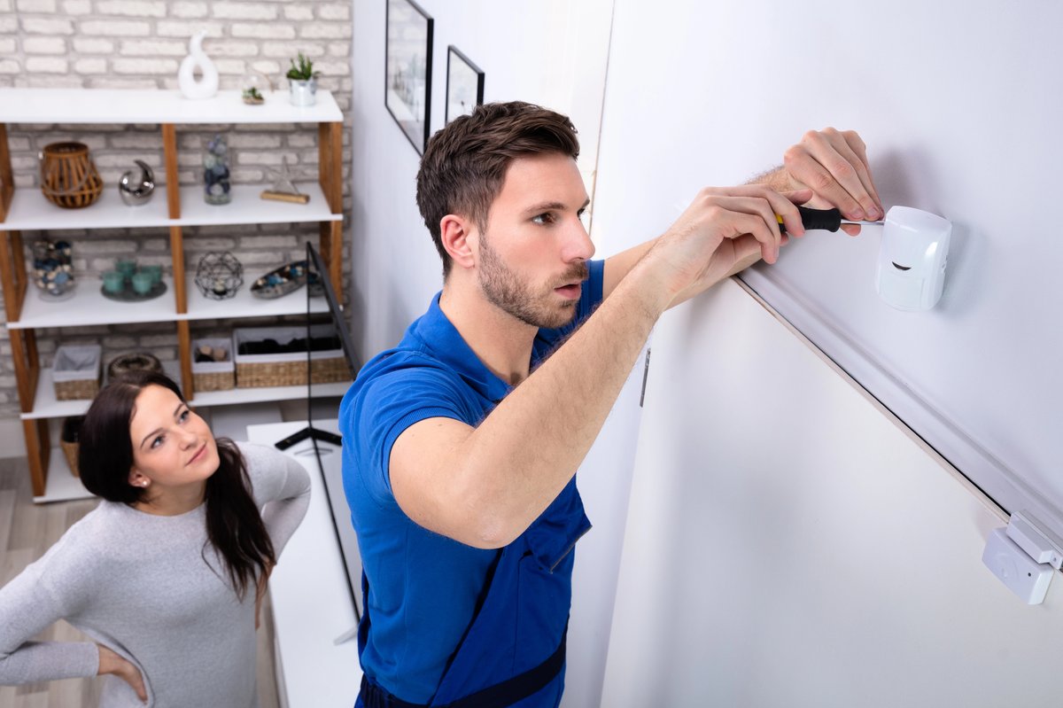 Technicien installant un détecteur de mouvement dans une maison à Colmar pendant qu'une cliente supervise l'installation du système d’alarme.