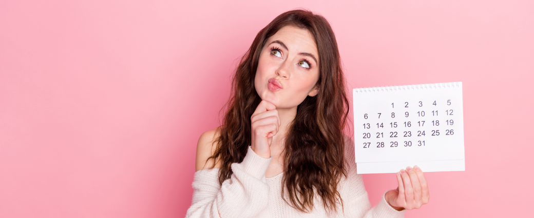 A young woman with long dark hair holds a calendar in one hand and scratches her chin as if she is making a decision.