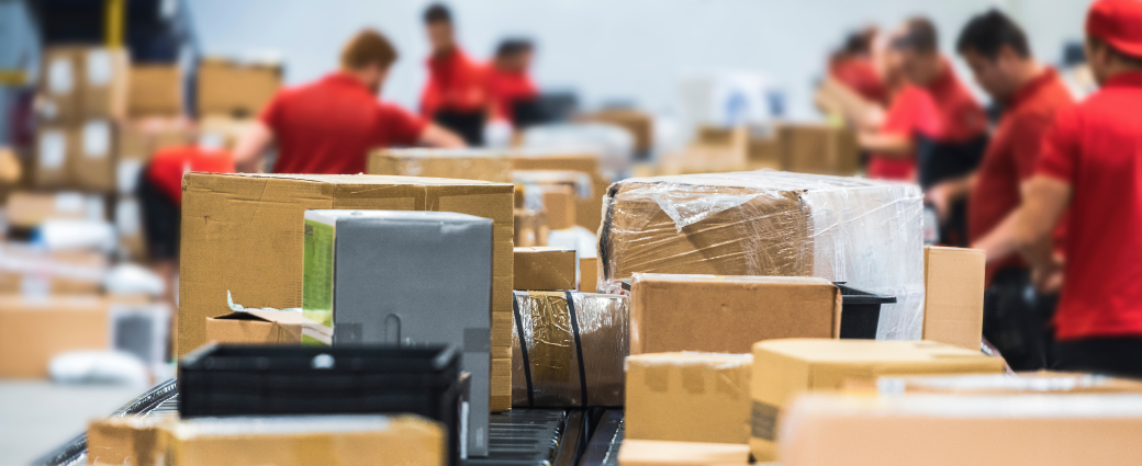 Workers in red shirts sort packages of various sizes on a conveyor belt in a warehouse