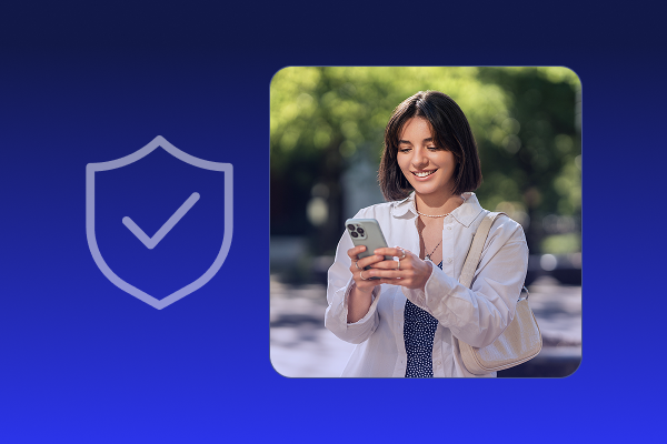 A young woman smiling while looking at her smartphone outdoors with a blurred green background and a translucent shield icon with a check mark on the left, symbolizing security.