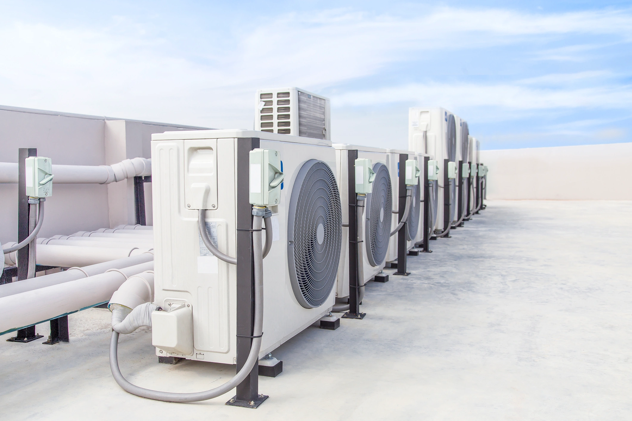 A row of HVAC units on a rooftop under a clear blue sky.
