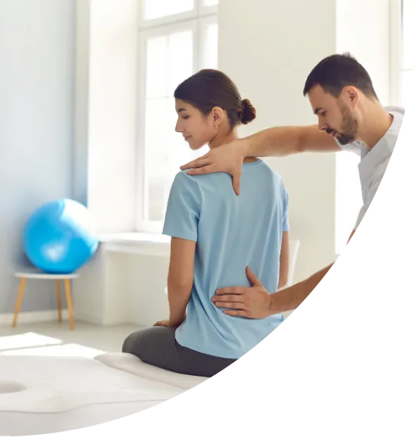 A physical therapist assessing a seated woman's back and shoulder posture in a bright, modern clinic setting.