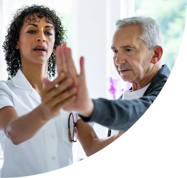 A healthcare professional guiding an elderly man through a physical therapy or rehabilitation exercise in a bright clinical setting.