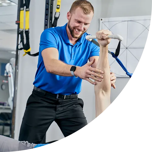 A physical therapist in a blue polo shirt assists a patient with an overhead rehabilitation exercise using a resistance pulley system.