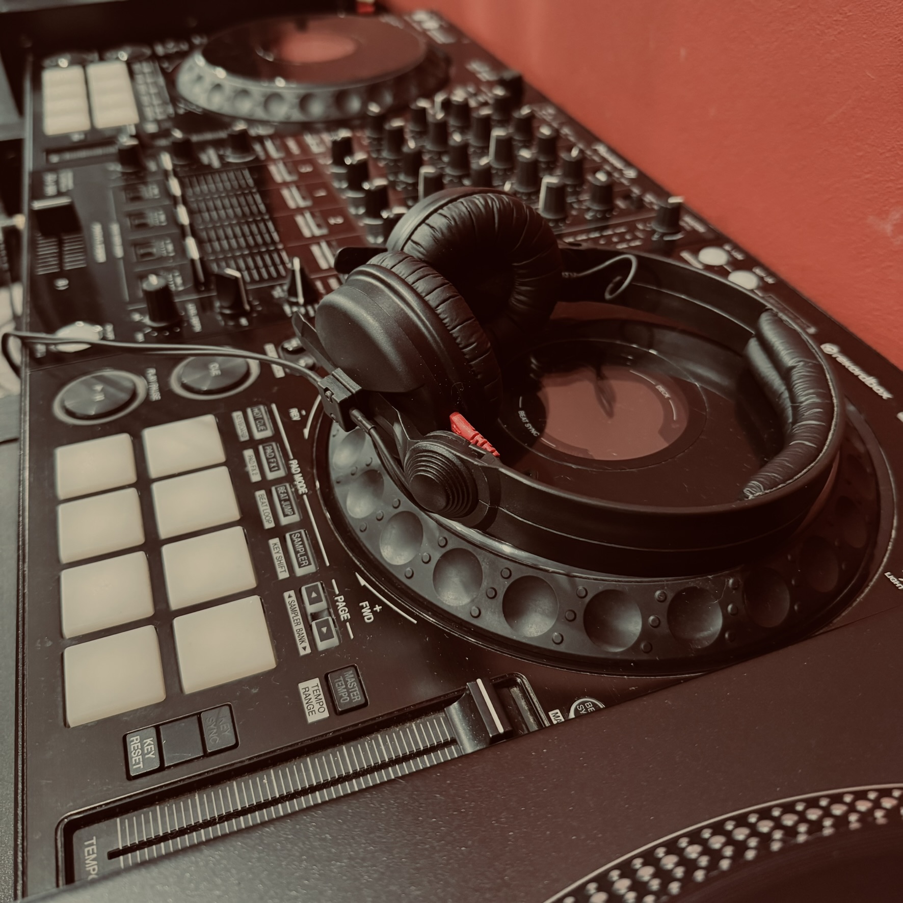 Black DJ controller with headphones resting on a jog wheel against a red background.