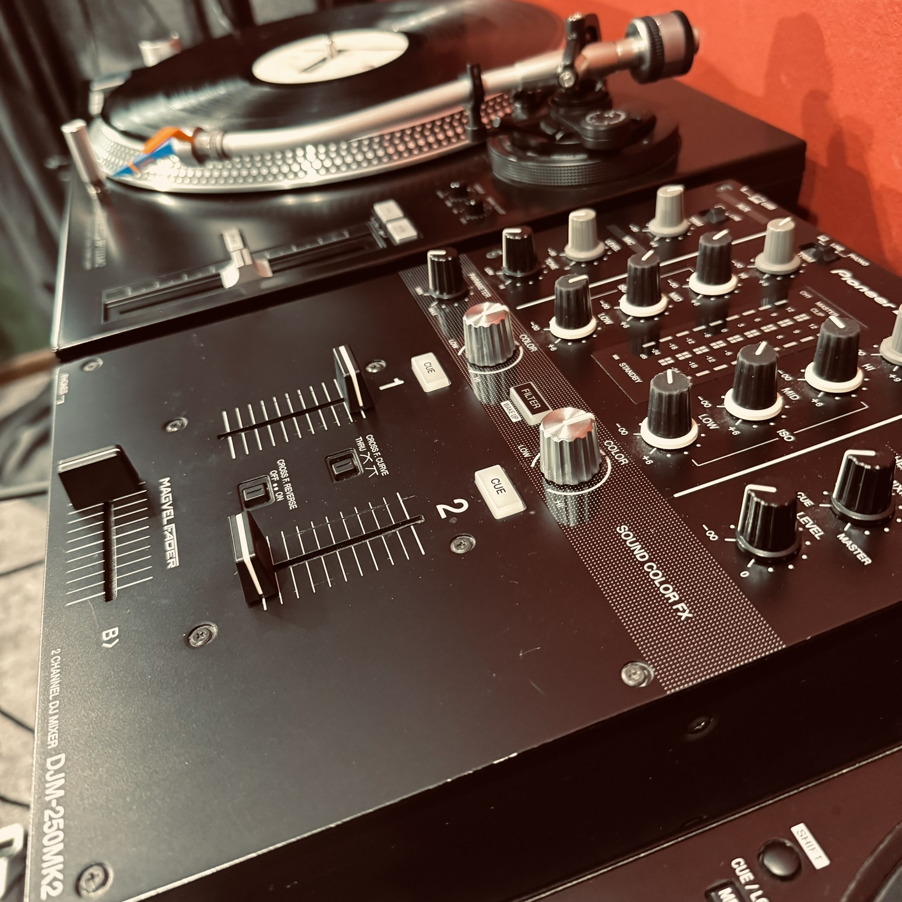 Close-up of a DJ setup featuring a turntable with a vinyl record and a DJ mixer with multiple knobs, sliders, and buttons.