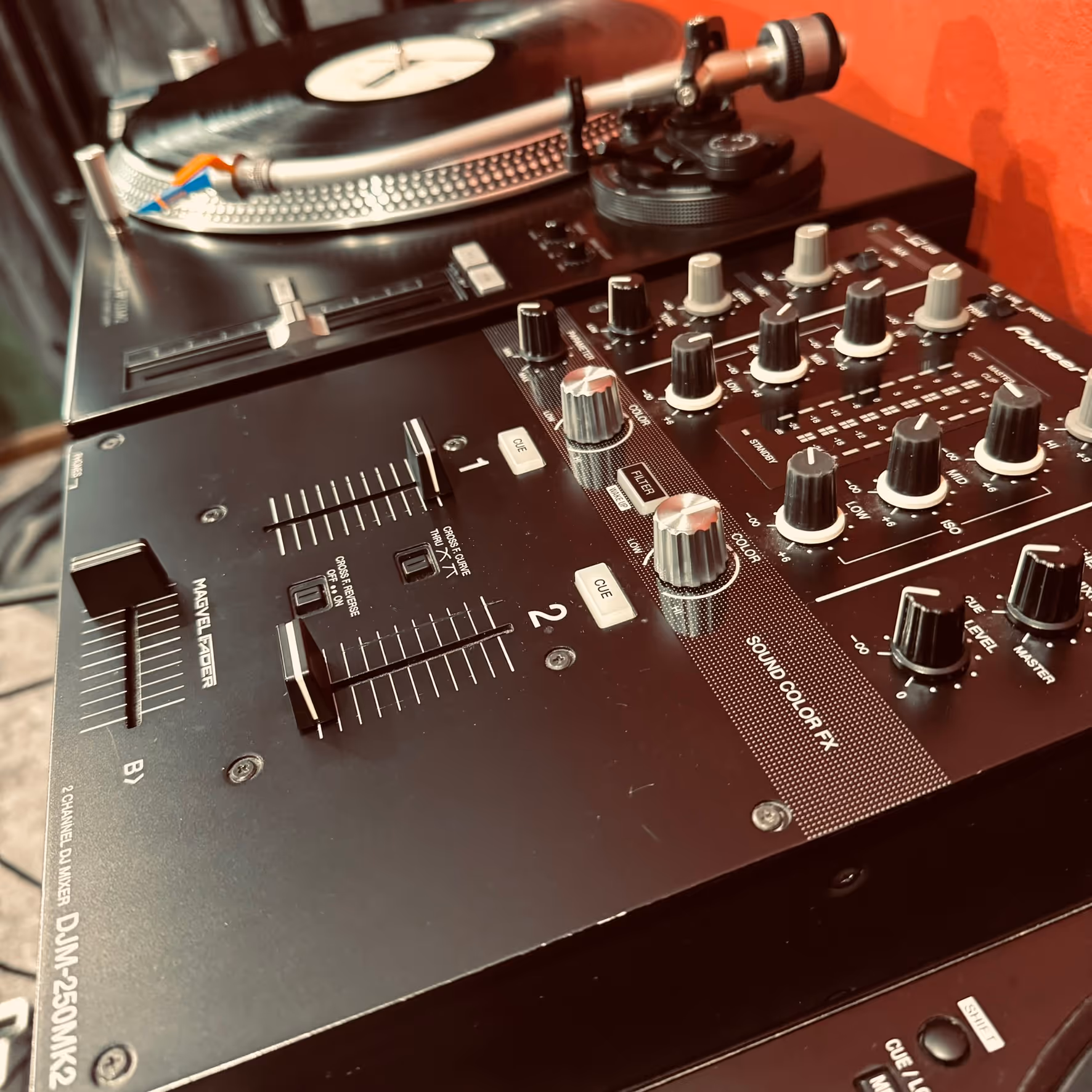 Close-up of a DJ setup featuring a turntable with a vinyl record and a DJ mixer with multiple knobs, sliders, and buttons.