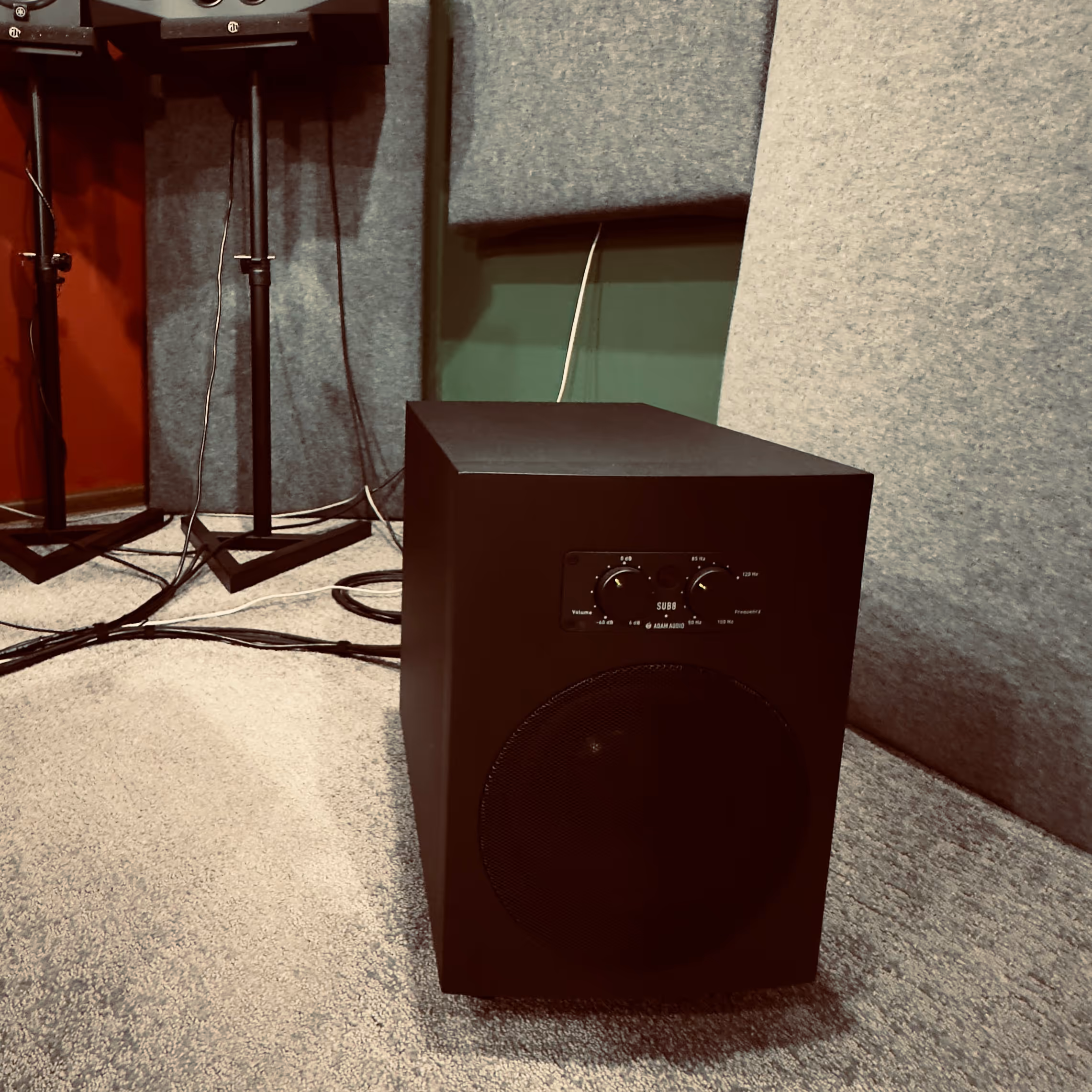 Tabby cat sitting on a drum throne in front of an electronic drum set in a music room.