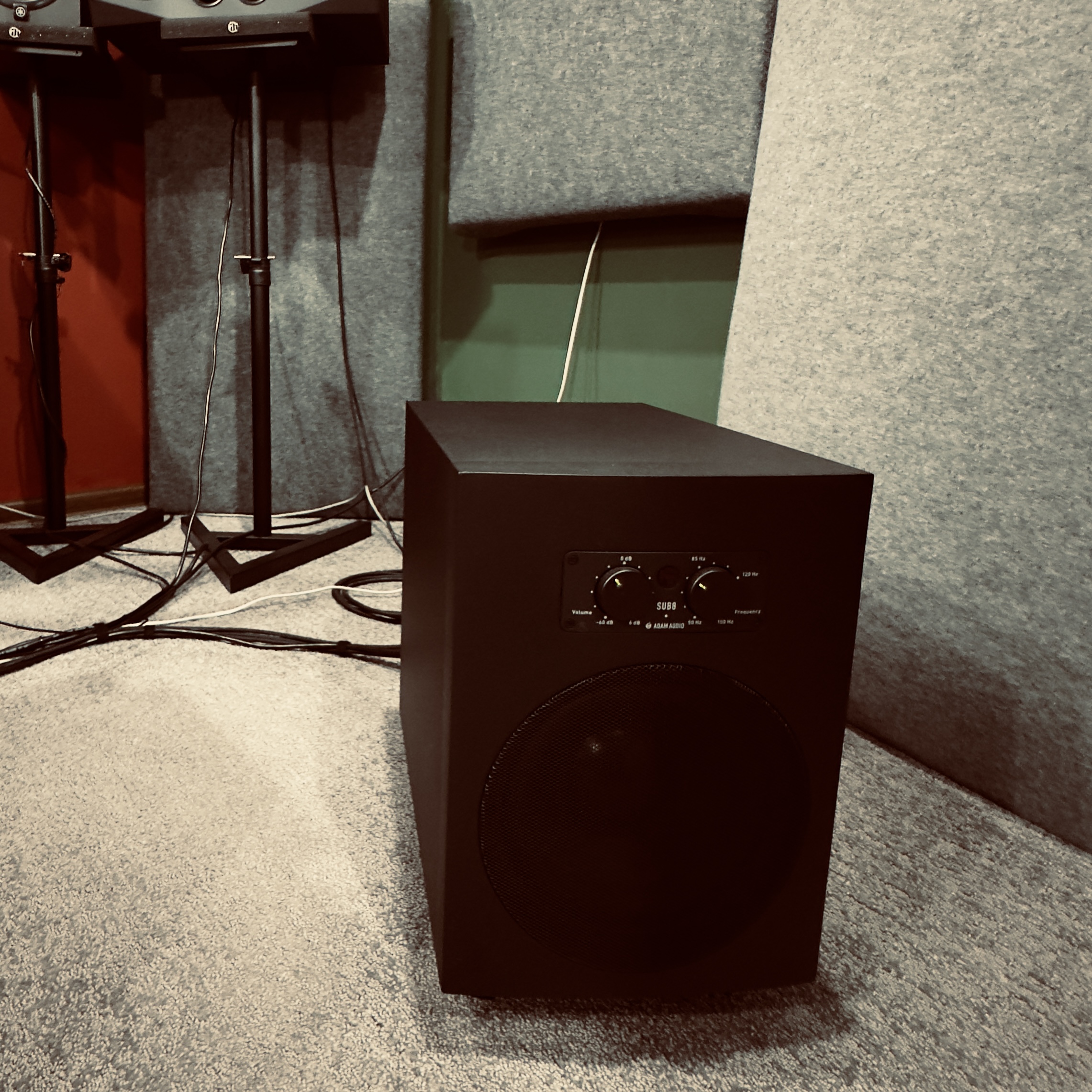 Tabby cat sitting on a drum throne in front of an electronic drum set in a music room.