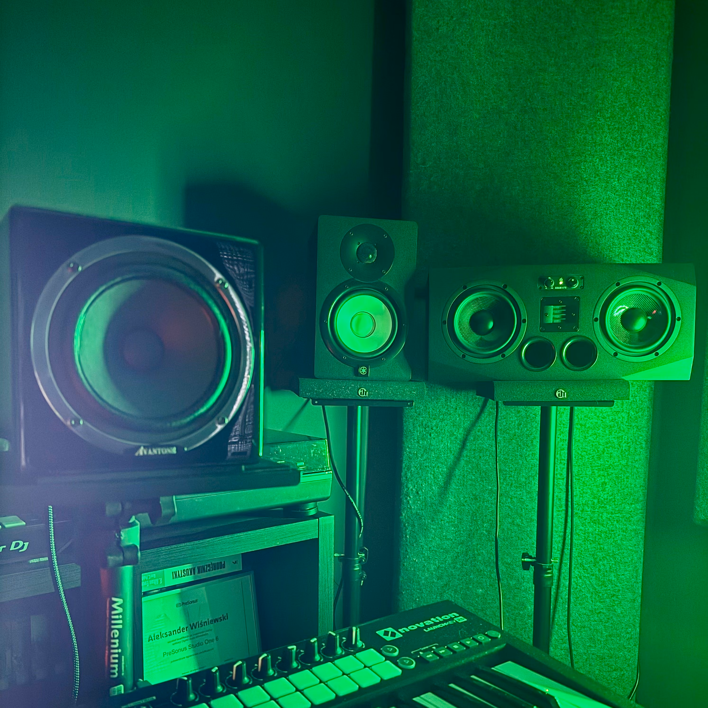 Podcast or music production desk with a professional microphone, headphones, music sampler, studio monitors, and computer screens in a room with plants and red walls.