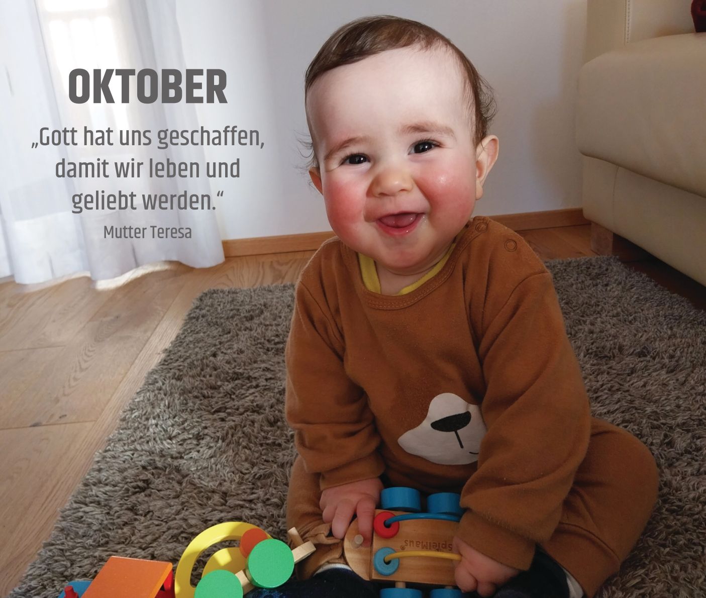 Ein lachendes Baby spielt auf dem Teppich im Wohnzimmer vor der Couch.