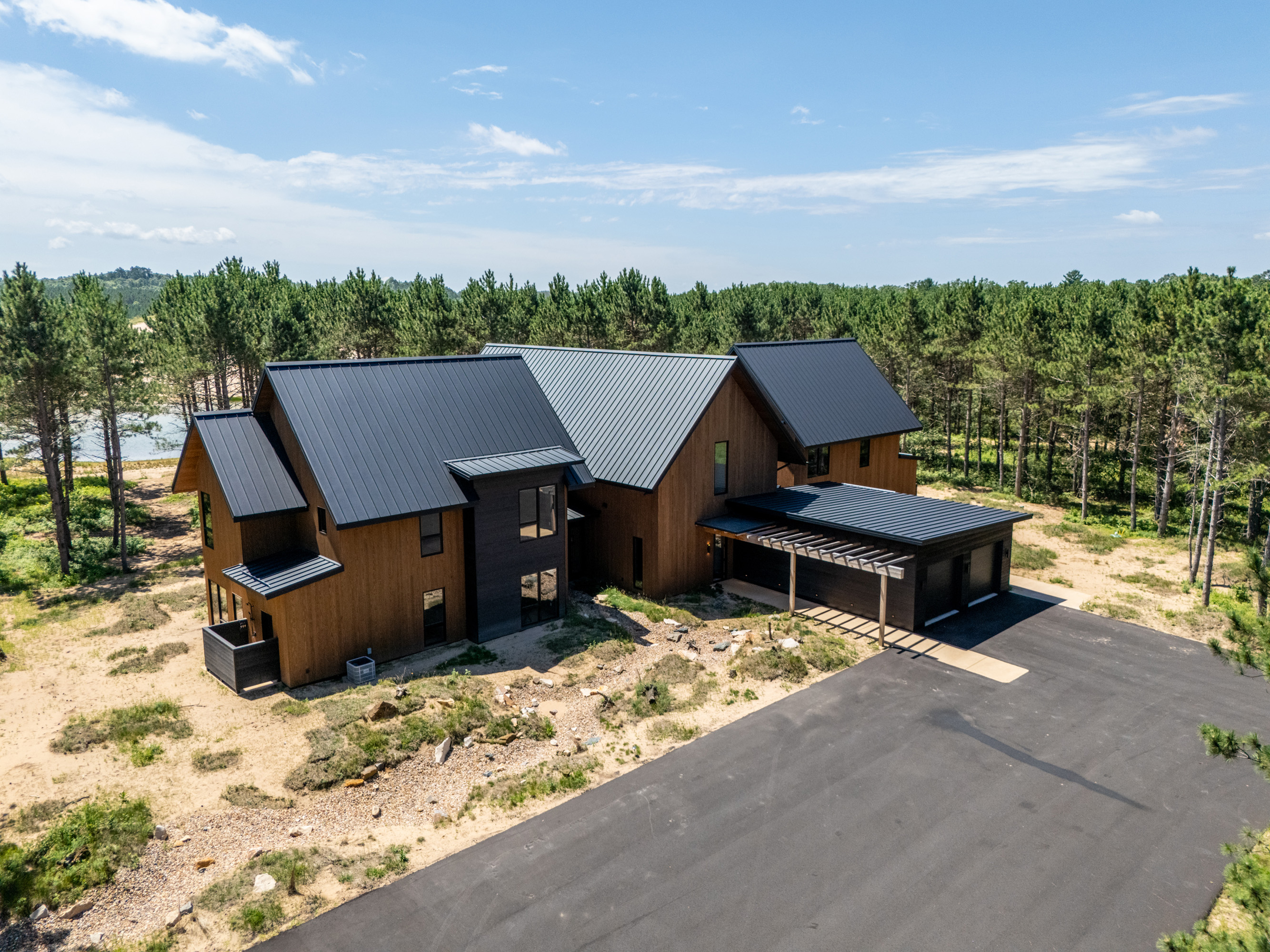 Modern wood-sided home with black metal roofs surrounded by pine trees.