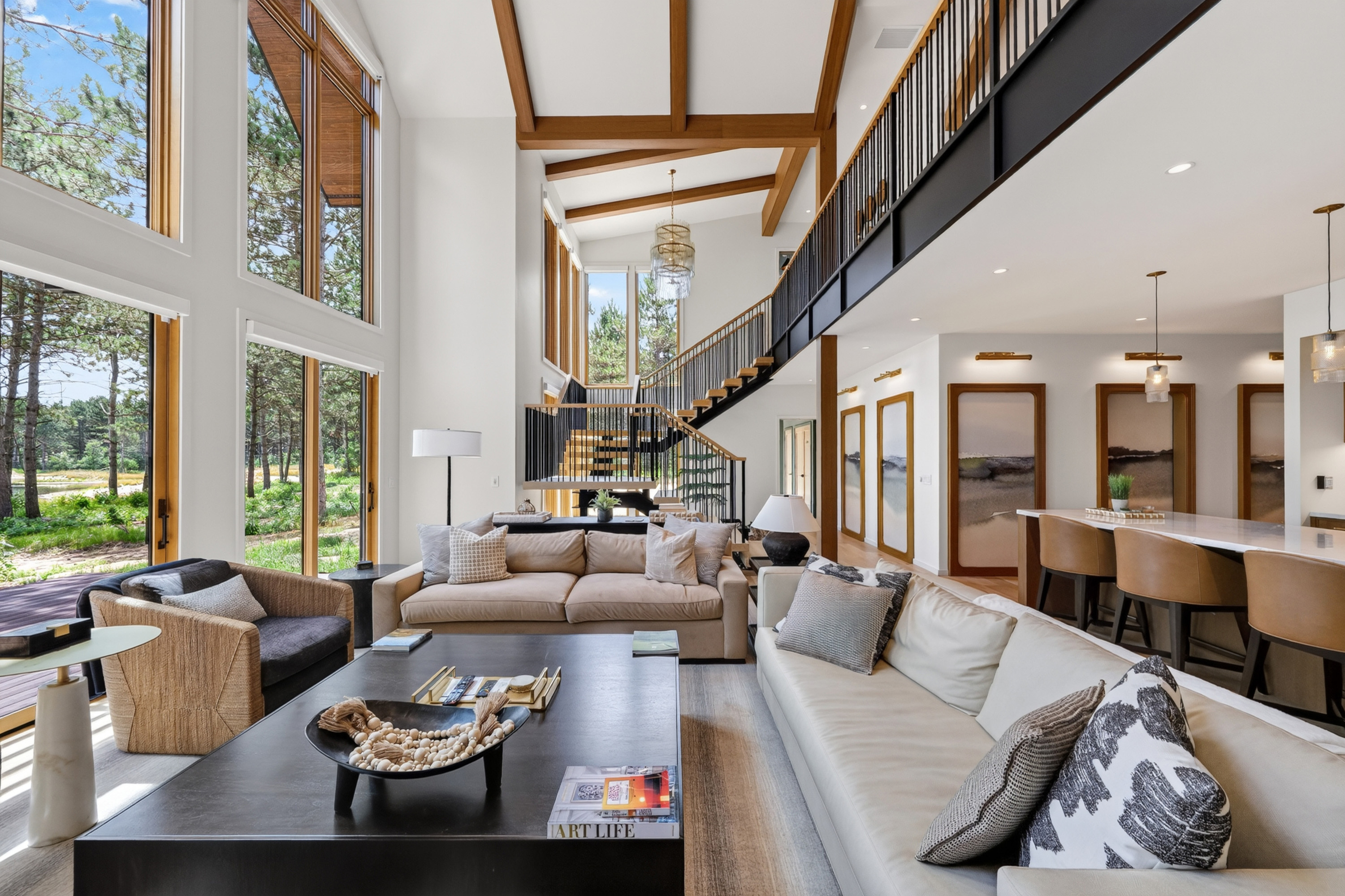 Open living room with large windows, sofas, staircase, and adjacent bar seating.