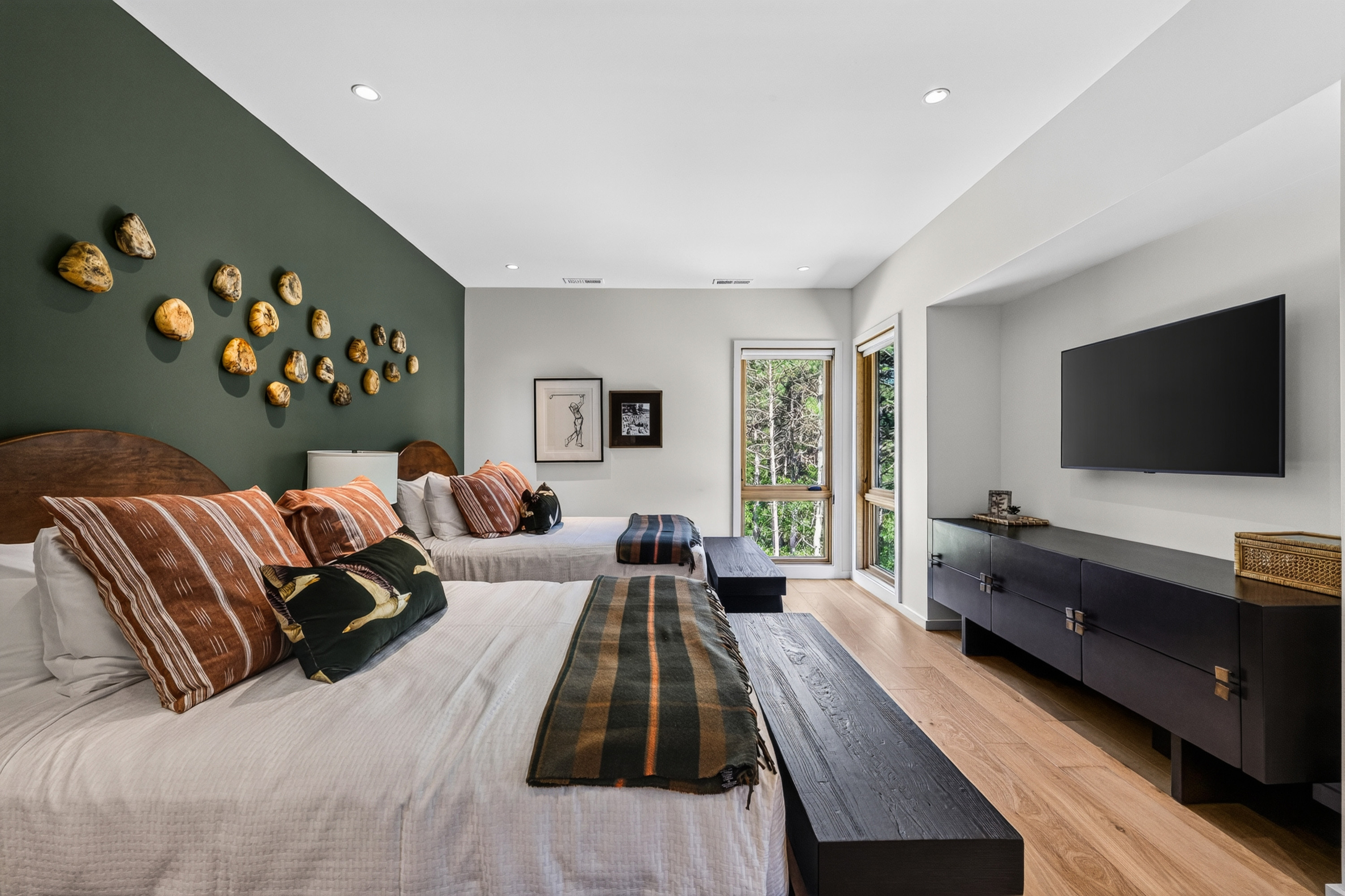 Bedroom with two beds, green accent wall, wall-mounted TV, and forest views.