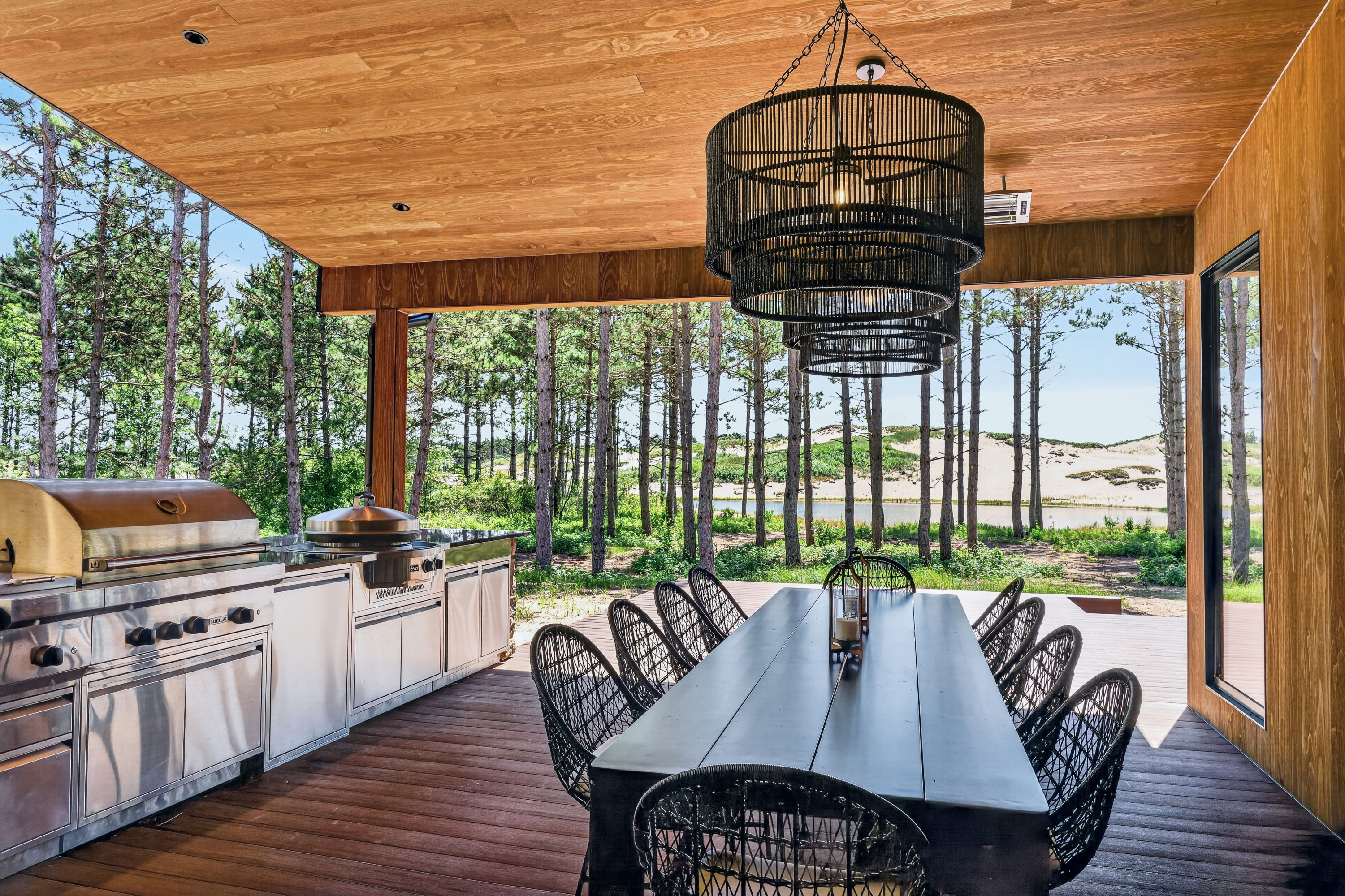 Covered outdoor dining area with built-in grills overlooking trees and water.