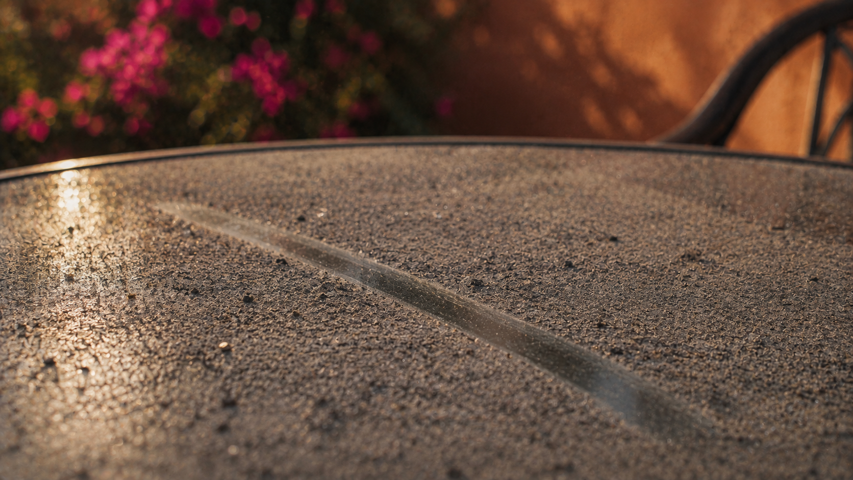 Fine gray ash settled across a glass patio table with a single fingertip line drawn through it.