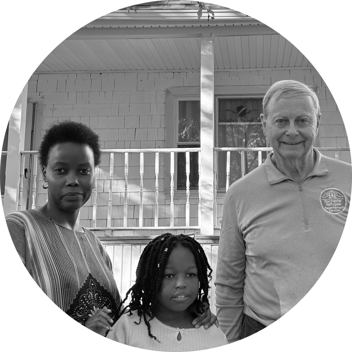 A woman and a girl standing beside a man in front of a house with a porch
