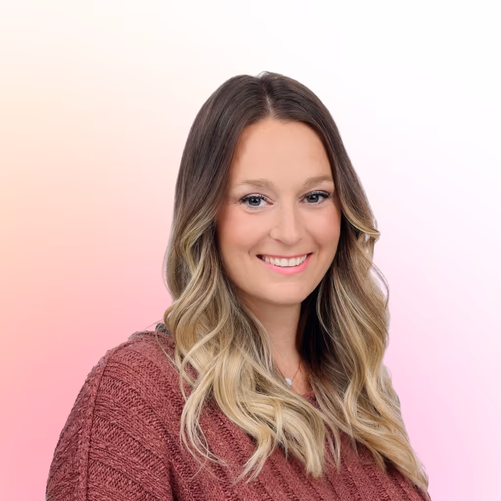 Smiling woman with long wavy blonde hair wearing a pink knit sweater against a soft gradient background.