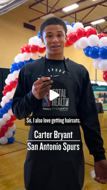 Carter Bryant of the San Antonio Spurs speaking at an NBA Total Health event beside a red, white and blue balloon arch, captioned: So, I also love getting haircuts.